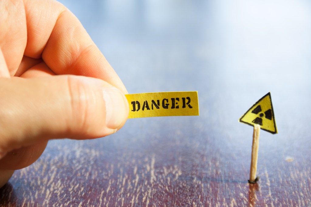 A hand holding a yellow sign labeled 'DANGER' next to a small triangular radioactive hazard sign.