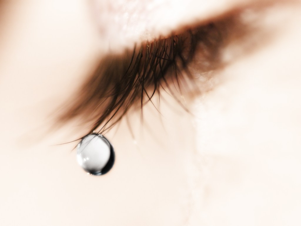 Close-up of a female eye with a tear drop hanging from the eyelashes.