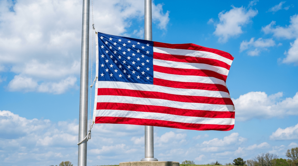 American flag at half-staff on a metal pole with a blue cloudy sky background