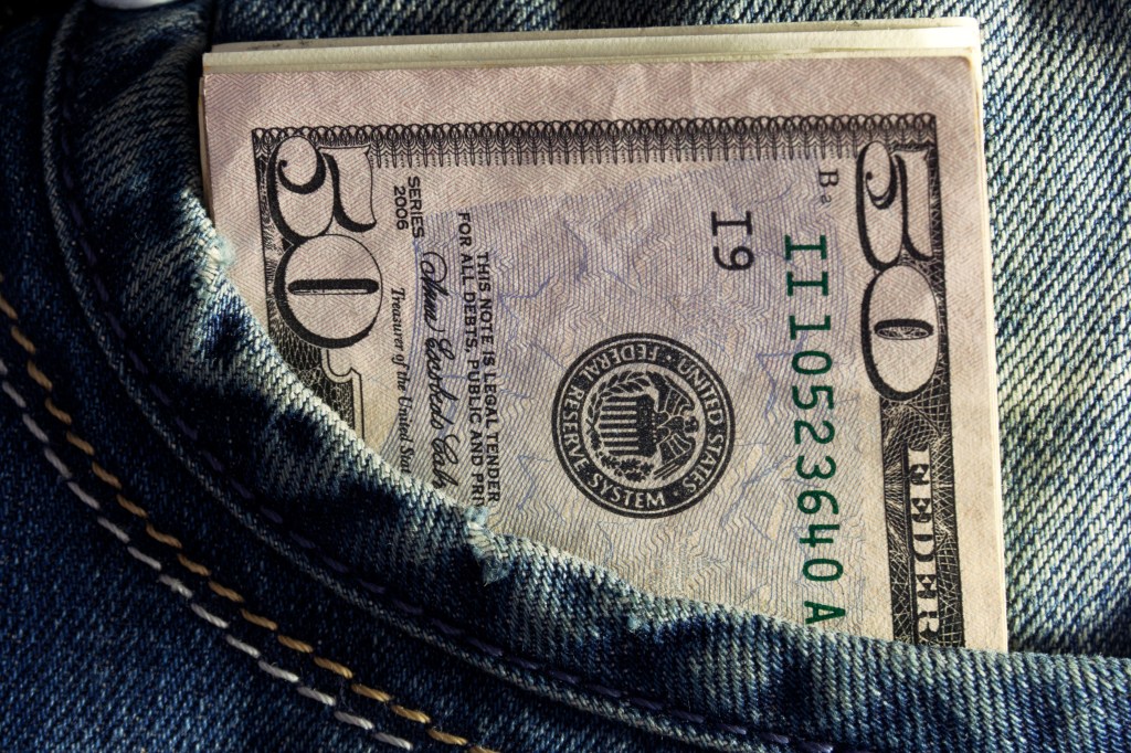 A fifty-dollar bill partially visible in a blue denim pocket.